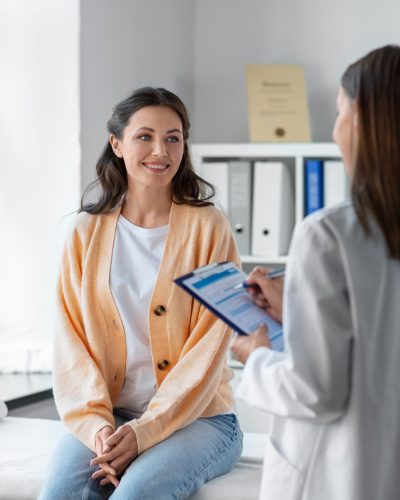 medicine, healthcare and people concept - female doctor with clipboard talking to smiling woman patient at hospital