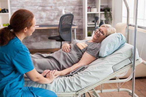 Female doctor in nursing home holding hand of old woman