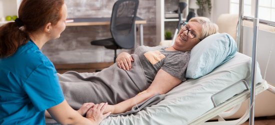 Female doctor in nursing home holding hand of old woman
