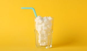 Glass with sugar cubes and straw on yellow background, space for text