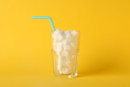 Glass with sugar cubes and straw on yellow background, space for text