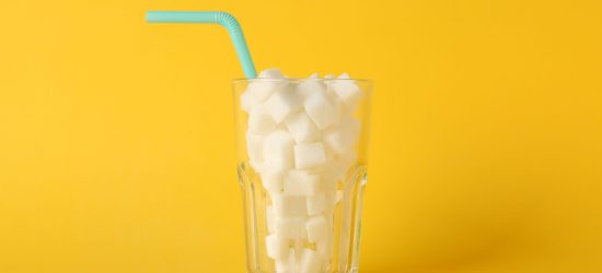 Glass with sugar cubes and straw on yellow background, space for text